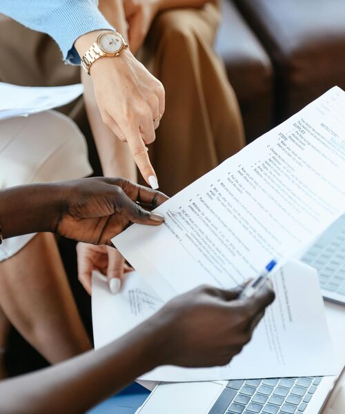 Mehrere Personen besprechen gemeinsam Dokumente, eine Hand zeigt dabei auf eine Textstelle auf einem Blatt Papier.
