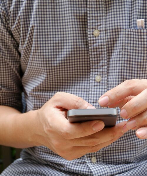 Person in kariertem Hemd hält ein Smartphone und tippt darauf.