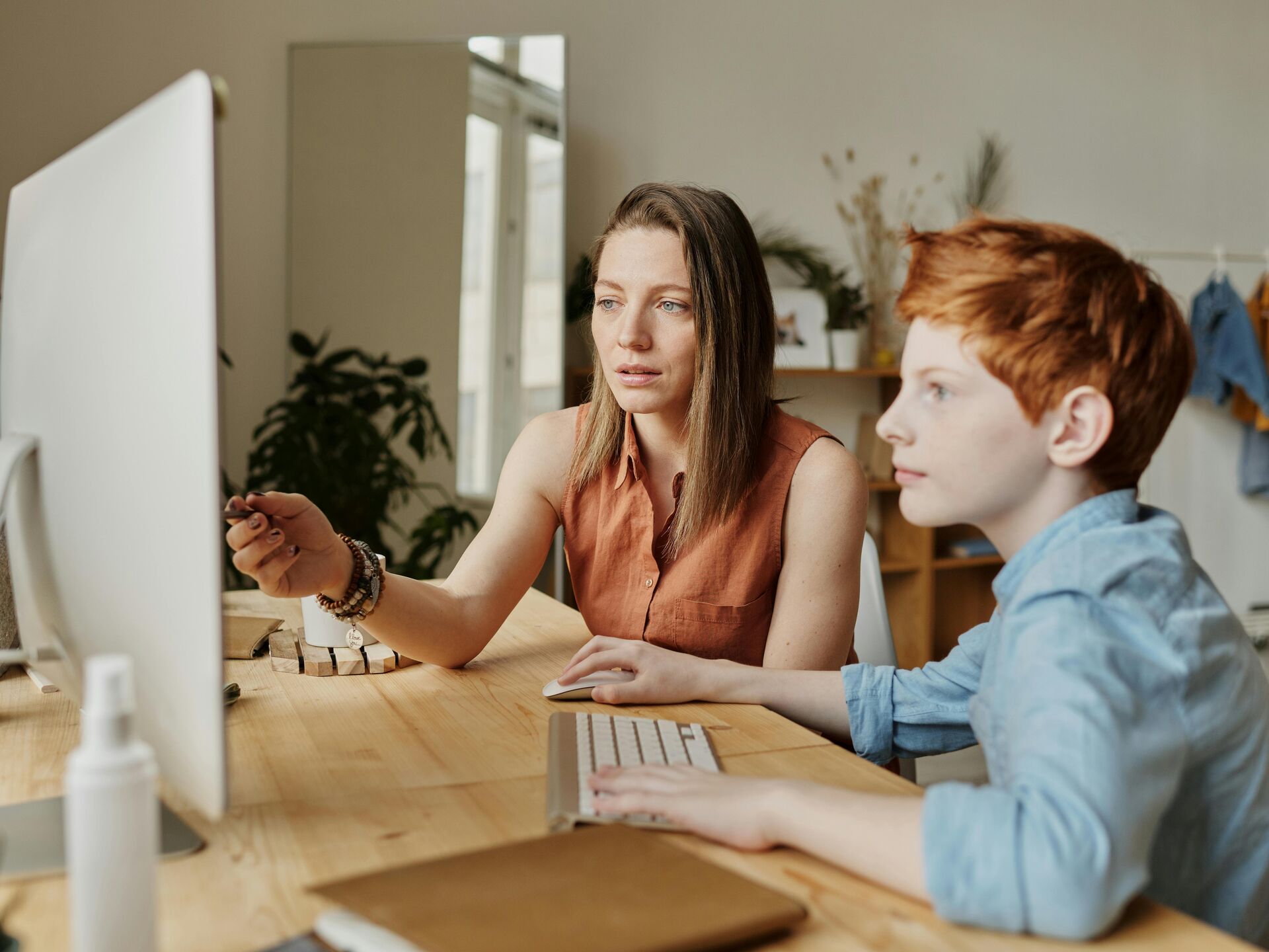 Eine Frau und ein Kind sitzen gemeinsam an einem Schreibtisch vor einem Computer und konzentrieren sich auf den Bildschirm.