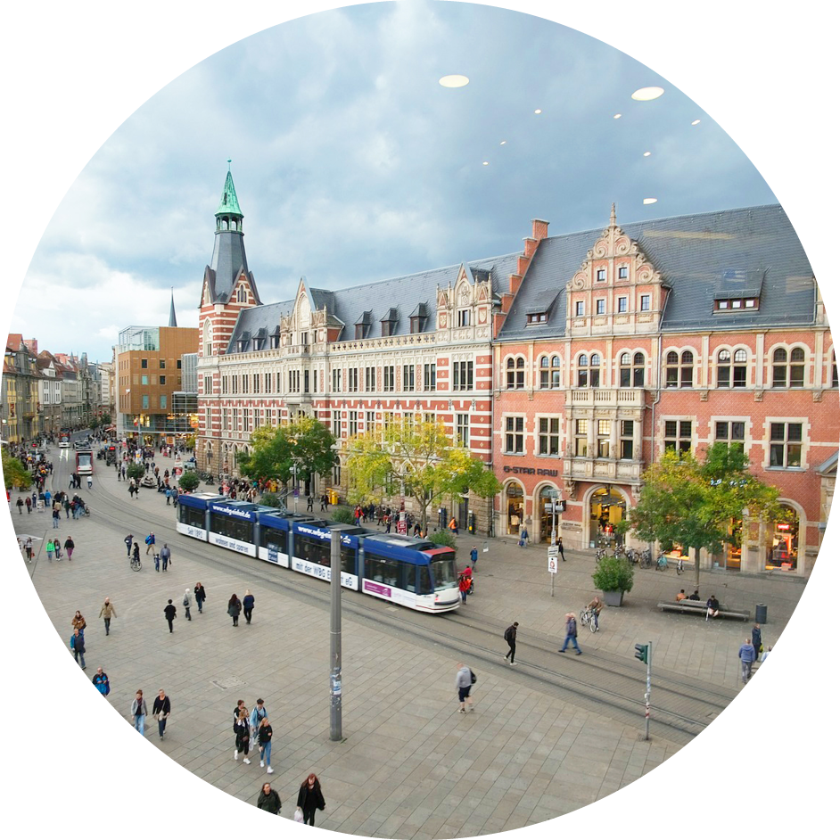 Belebte Innenstadt mit Straßenbahn und historischen Gebäuden unter wolkigem Himmel.