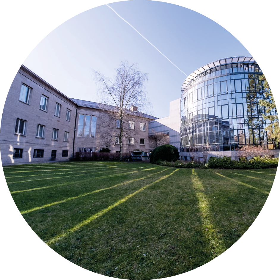 Moderne Gebäudekombination aus Glasfassade und Steinbau mit gepflegtem Rasen im Vordergrund.